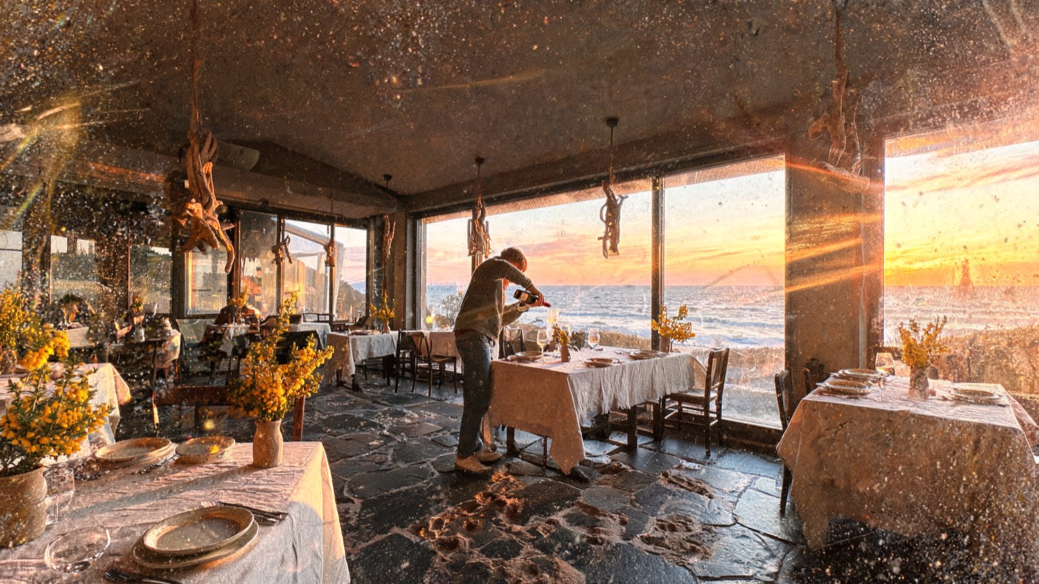 Coastal restaurant with linen-laid tables, driftwood pendant lights and tall windows to the sea at golden hour